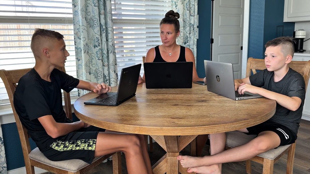 A mom and her two sons at the kitchen table, each working on a laptop