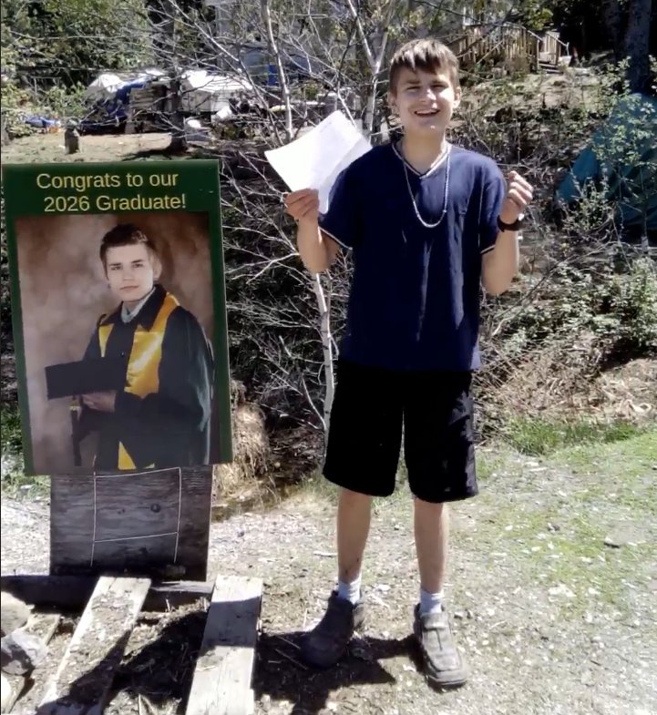 Hunter G. smiling and holding his acceptance letter beside a sign congratulating the 2026 graduate